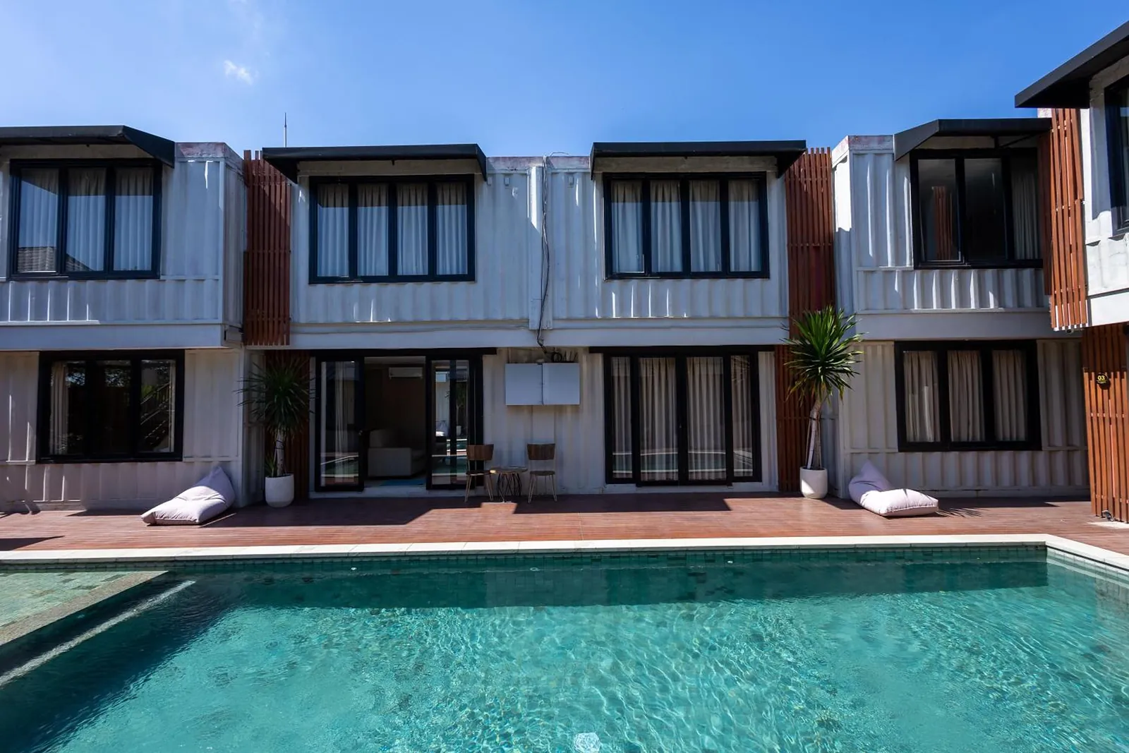 The pool in front of a row of two-storey container suites with tall black-framed windows