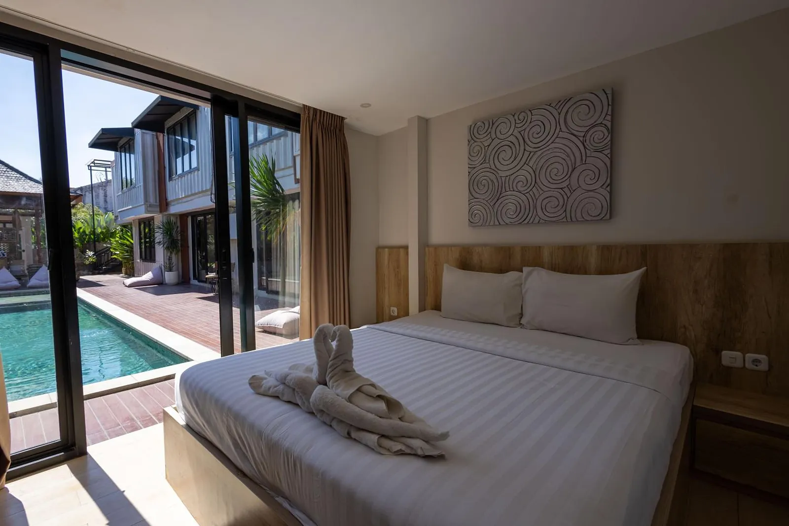 Deluxe Studio: a king bed beside floor-to-ceiling glass that opens onto the pool deck